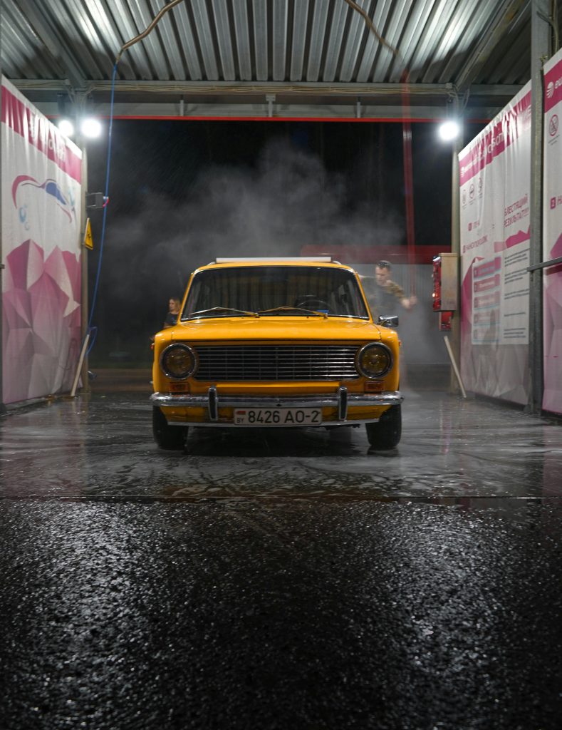 Classic yellow car being cleaned at night in a self-service car wash.